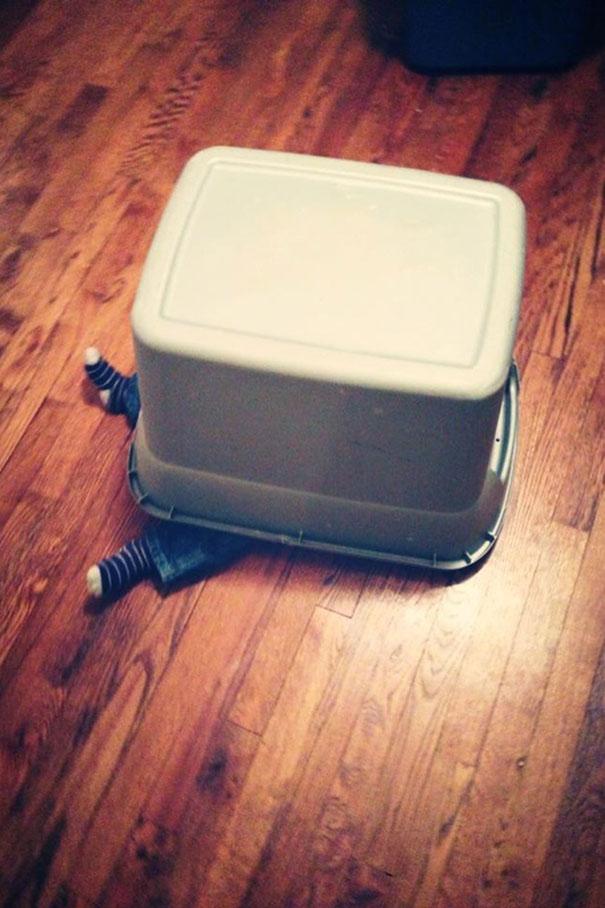 Child hiding under a plastic bin with feet sticking out