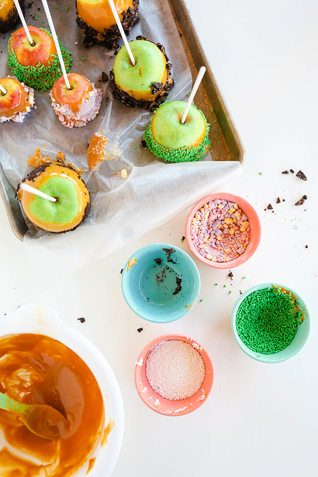 caramel apples dipped in candy setting on tray