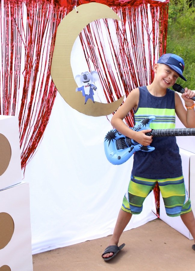 boy-wearing-a-hat-and-holding-a-guitar-siniging-on-a-microphone-with-a-diy-mini-stage