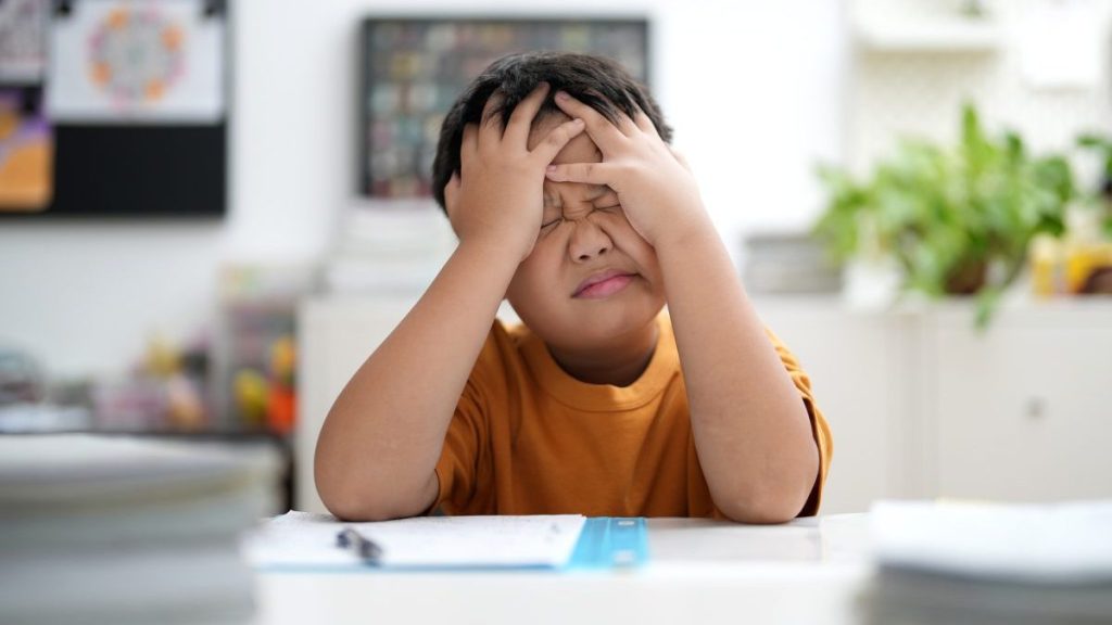 Young Asian boy is tired of doing homework, sitting at the table.