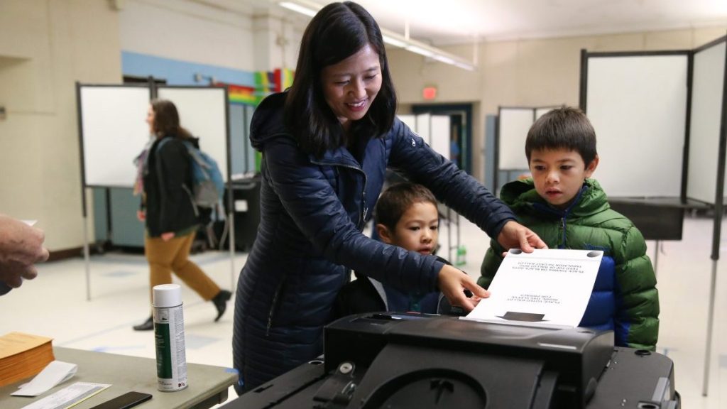 Boston Mayor Michelle Wu places her ballot into the machine at the Bates School, as her two sons looked on.