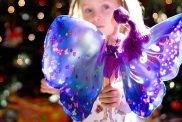 A three year old girl on Christmas morning in front of a Christmas tree with her new fairy doll. Background is filled with colorful Christmas tree lights.