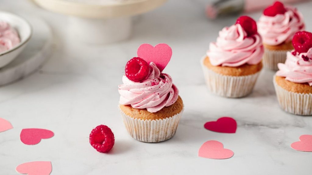 Freshly made raspberry cupcakes on kitchen counter. Delicious looking pink cupcakes with raspberry and paper heart topping.