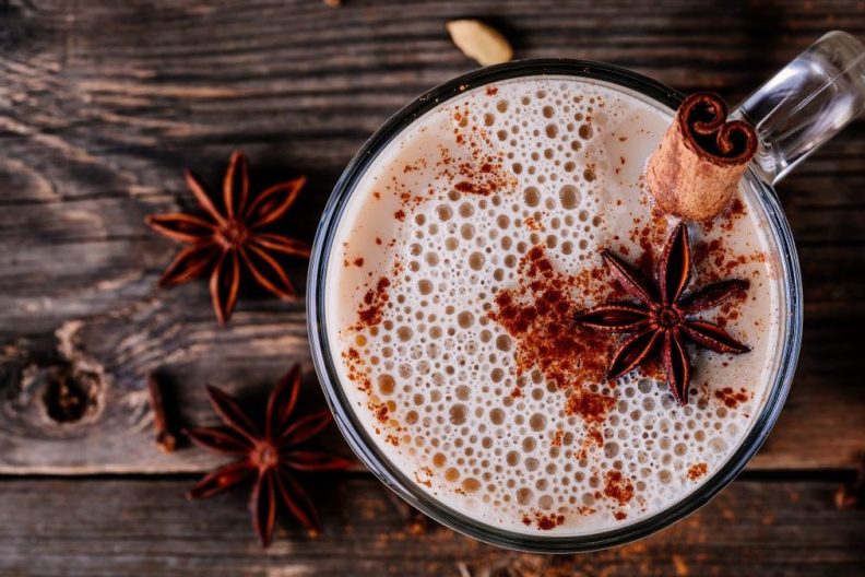 Homemade Hot Spiced Milk with anise and cinnamon stick in glass mug on wooden rustic background.