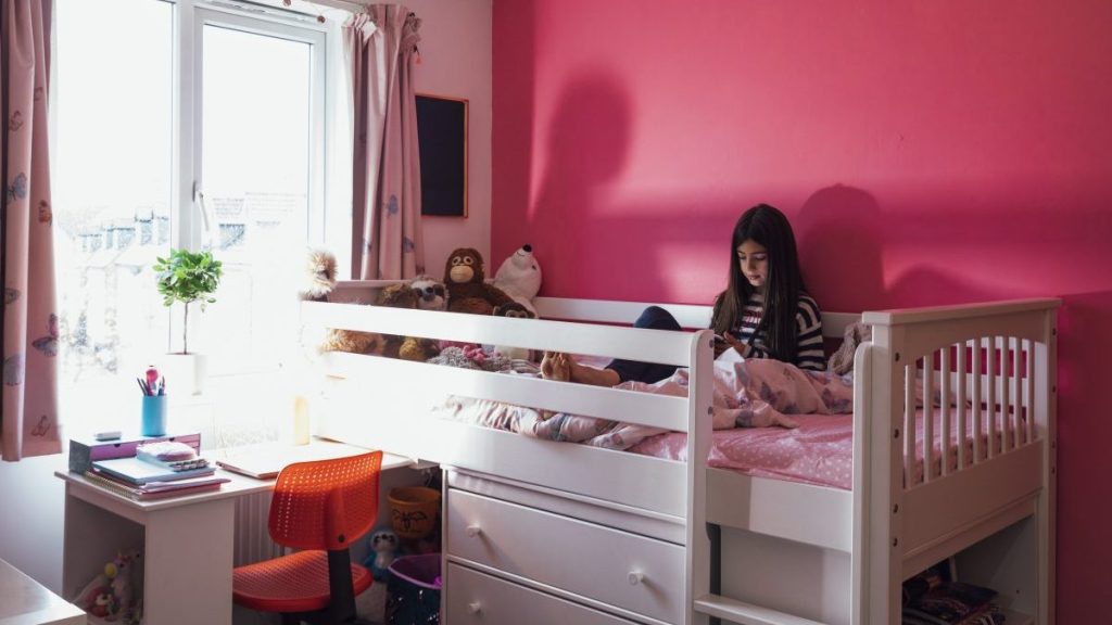 A little girl sitting in her princess pink bedroom in the North East of England engrossed in her phone on her elevated bunk bed chatting with friends using her mobile phone.