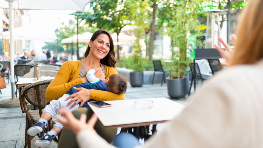 Young mother breastfeeding her baby boy in public while sitting in a cafe with her mother.