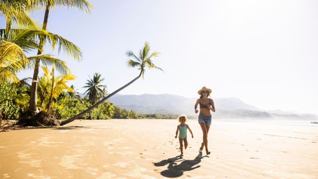 A mother and her daughter running down a palm tree scattered beach in Costa Rica.