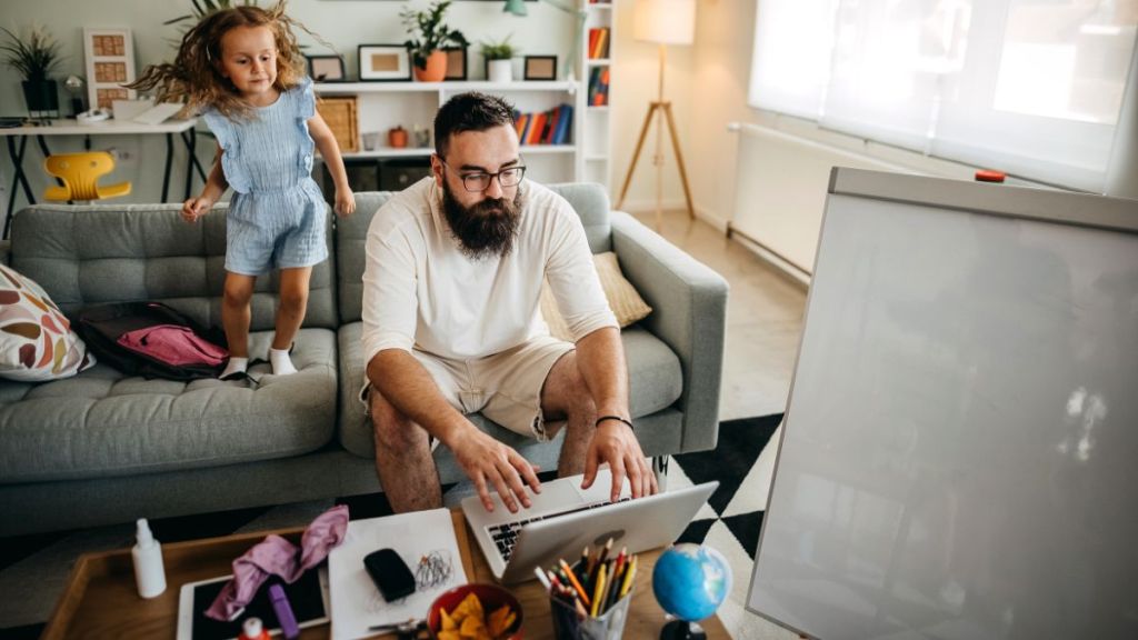 Father and daughter spending time together at home while he works hard.