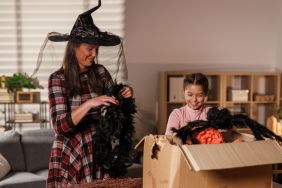 Candid shot of mid adult woman and her daughter discovering Halloween decorations that they are unpacking from a cardboard box before decorating their home.