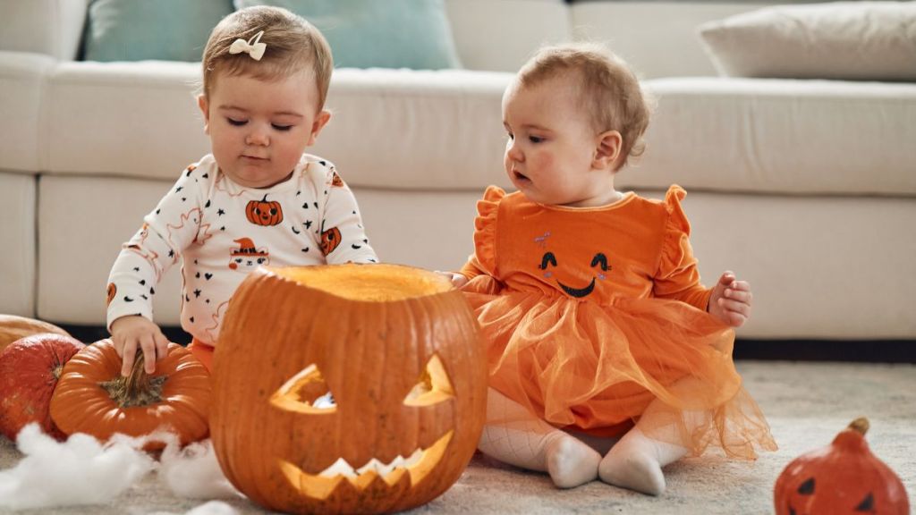 Twin sisters on Halloween day. They are indoors with a pumpkins, playing around.