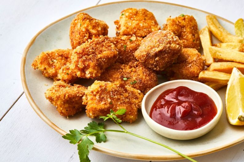 Sweet potato turkey nuggets on a plate, with ketchup, french fries and lemon, served on a white wooden restaurant or home table