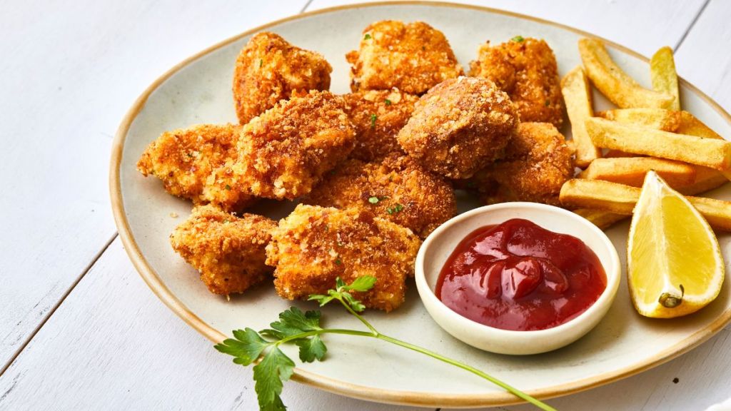 Sweet potato turkey nuggets on a plate, with ketchup, french fries and lemon, served on a white wooden restaurant or home table