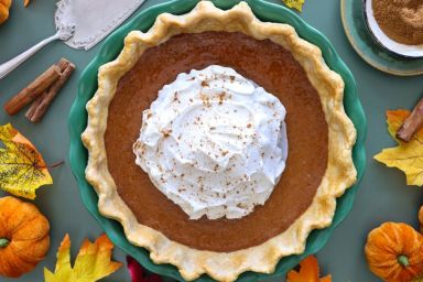 Stock photo showing close-up, elevated view of a tart tin case lined with freeform fluted, pastry that has been filled with a pumpkin puree to make a freshly baked pumpkin pie. Home baking concept.