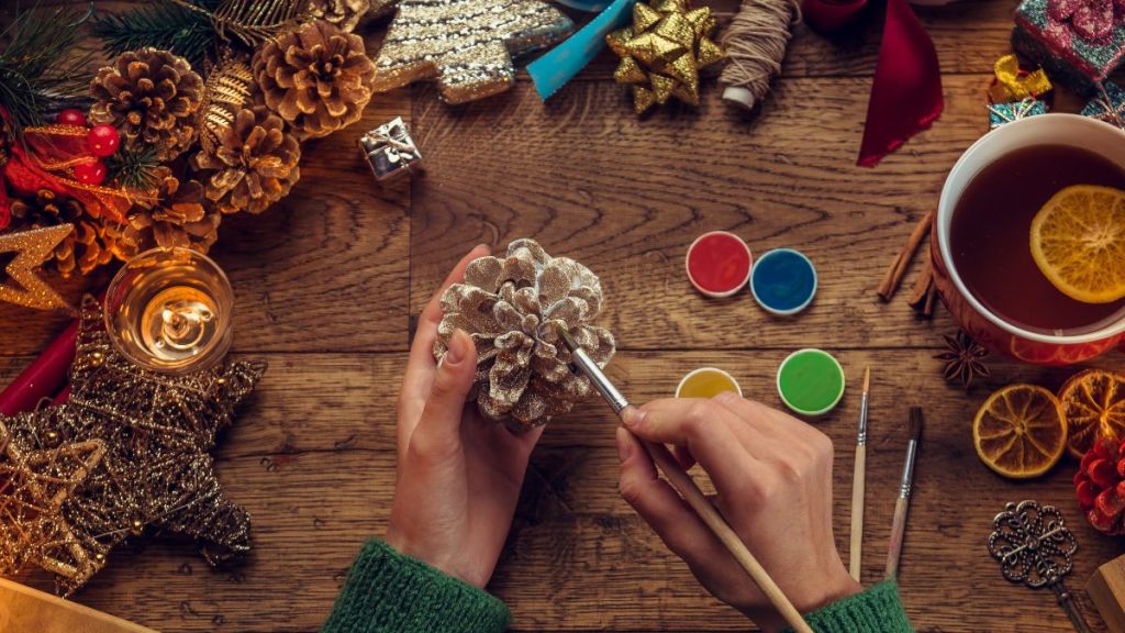 Individual doing DIY using pinecone while surrounded by craft materials and other quintessential fall items.