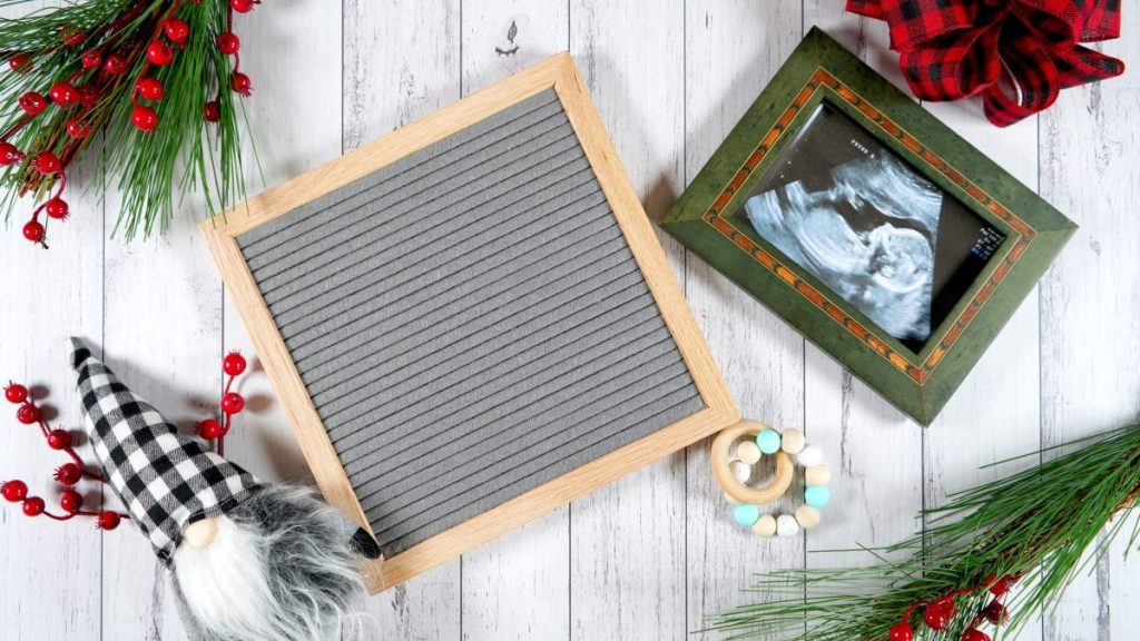 Baby pregnancy birth announcement letterboard mockup. Christmas farmhouse theme styled with gift with buffalo plaid bow and farmhouse style gnomes against a white wood background.