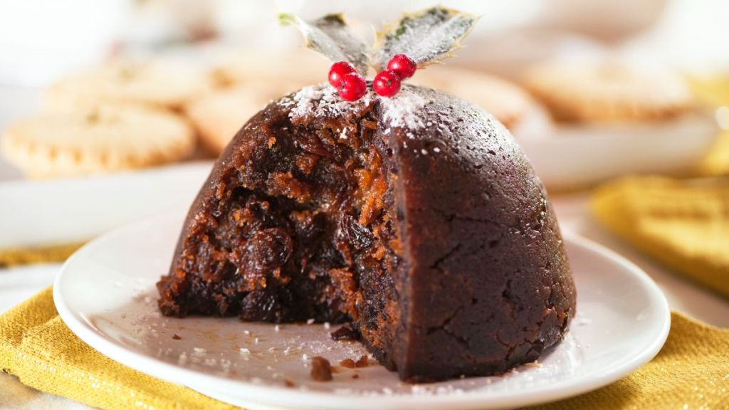 Christmas pudding with holly and mince pies in background and white and gold table colors.