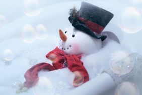 High key image of snowman wearing black top hat and red scarf in a bubble bath with bubbles in the air.