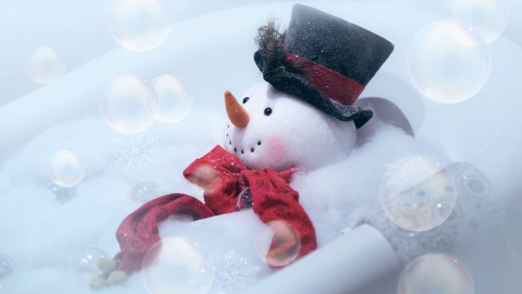 High key image of snowman wearing black top hat and red scarf in a bubble bath with bubbles in the air.