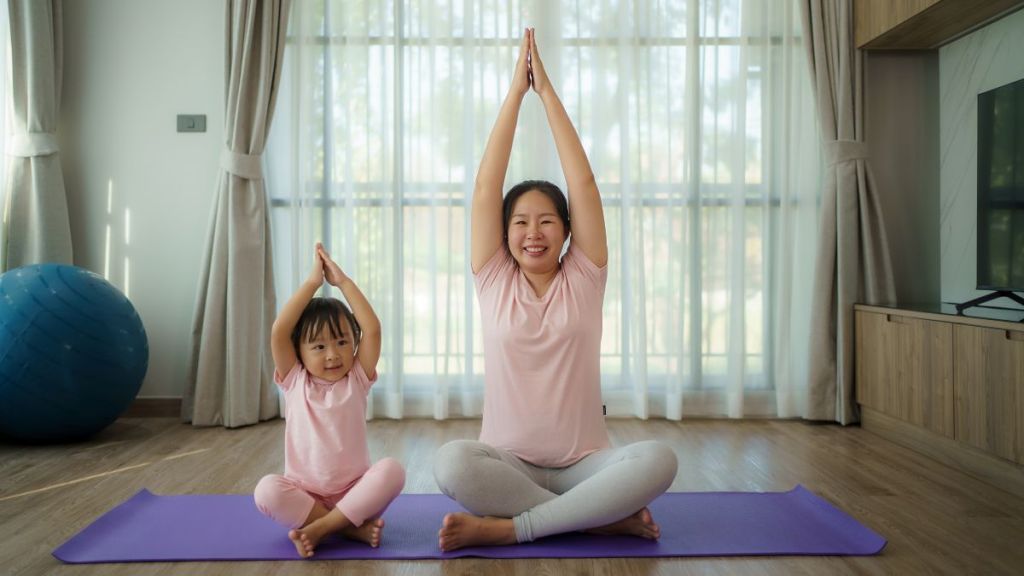 Asian young pregnant mother practicing yoga with daughter in living room at home.