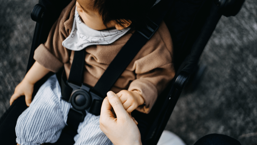 Mother holding baby girl's tiny hand who is sitting on stroller in park